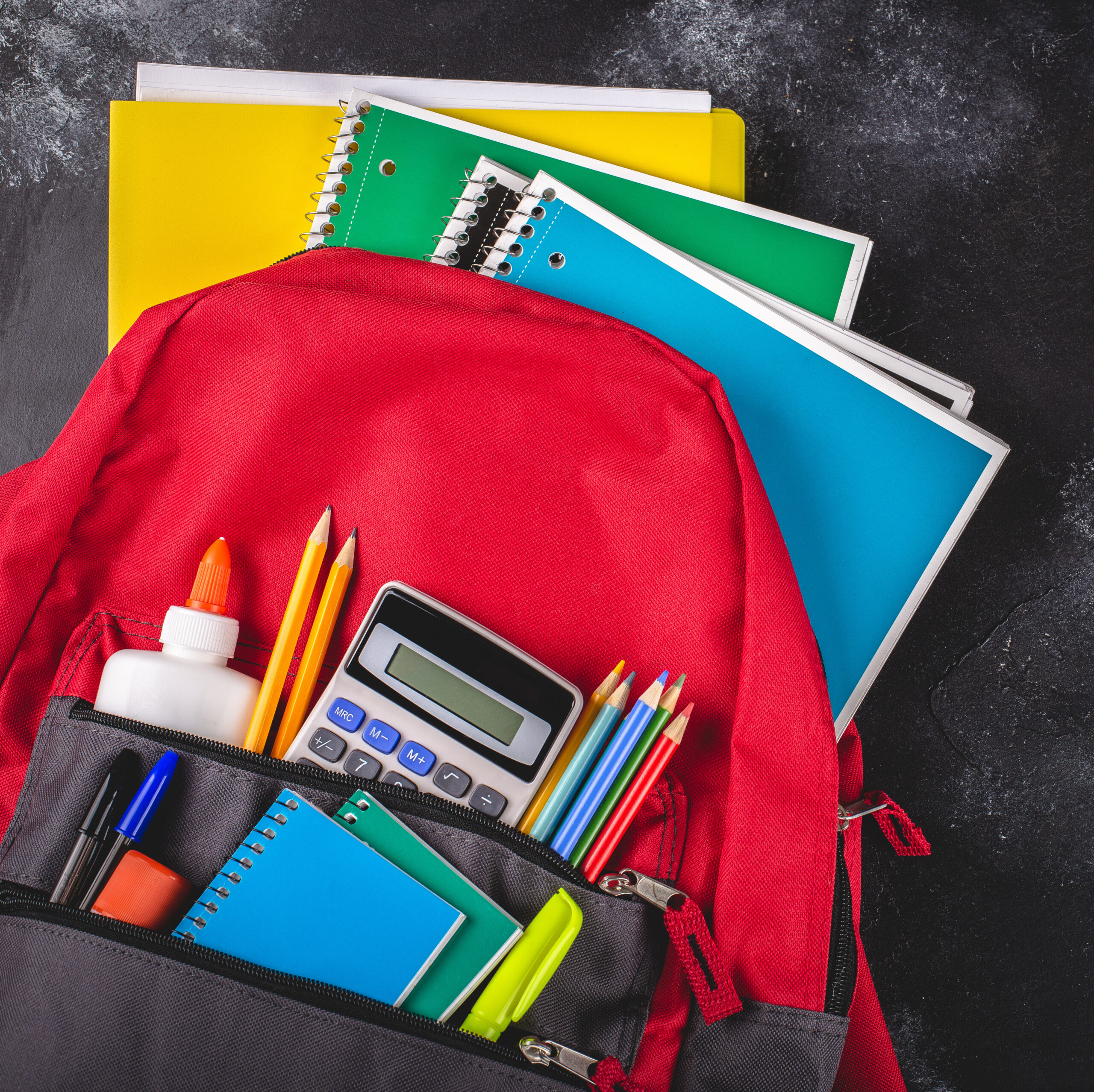 Backpack With School Supplies on a Blackboard Background